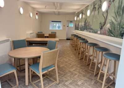 Queenswood common room with tables, chairs, and tropical mural