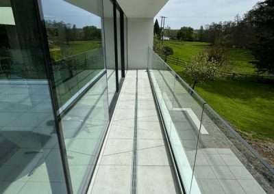 Modern balcony with glass railings overlooking a green field, complementing a shop cottage design.