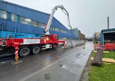 Red concrete pump truck with boom arm extended at Enersys Cell 2 Extension site.